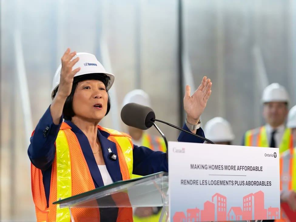 Olivia Chow in a hard hat and safety vest speaking at a “Making homes more affordable” podium