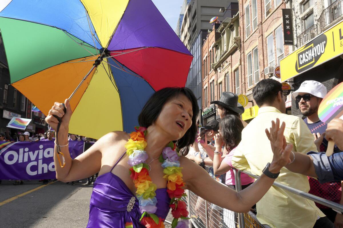 Olivia Chow at the Pride parade on Yonge Street holding a rainbow umbrella and high-fiving the crowd