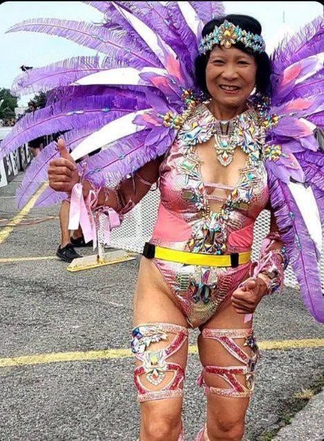 Olivia Chow in a purple-feathered carnival costume giving a thumbs-up on a Toronto street